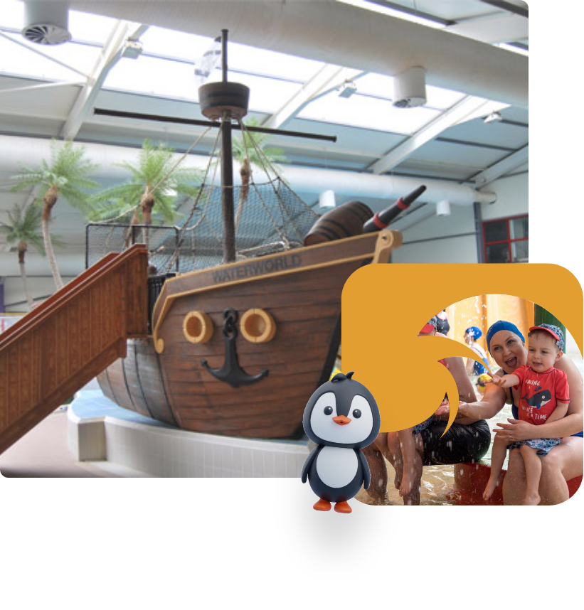 A woman and a toddler pose for a picture next to a pirate ship-themed water slide in an indoor water park. The scene features palm trees and an artificial sky backdrop, while a cartoon penguin stands in the bottom left corner.